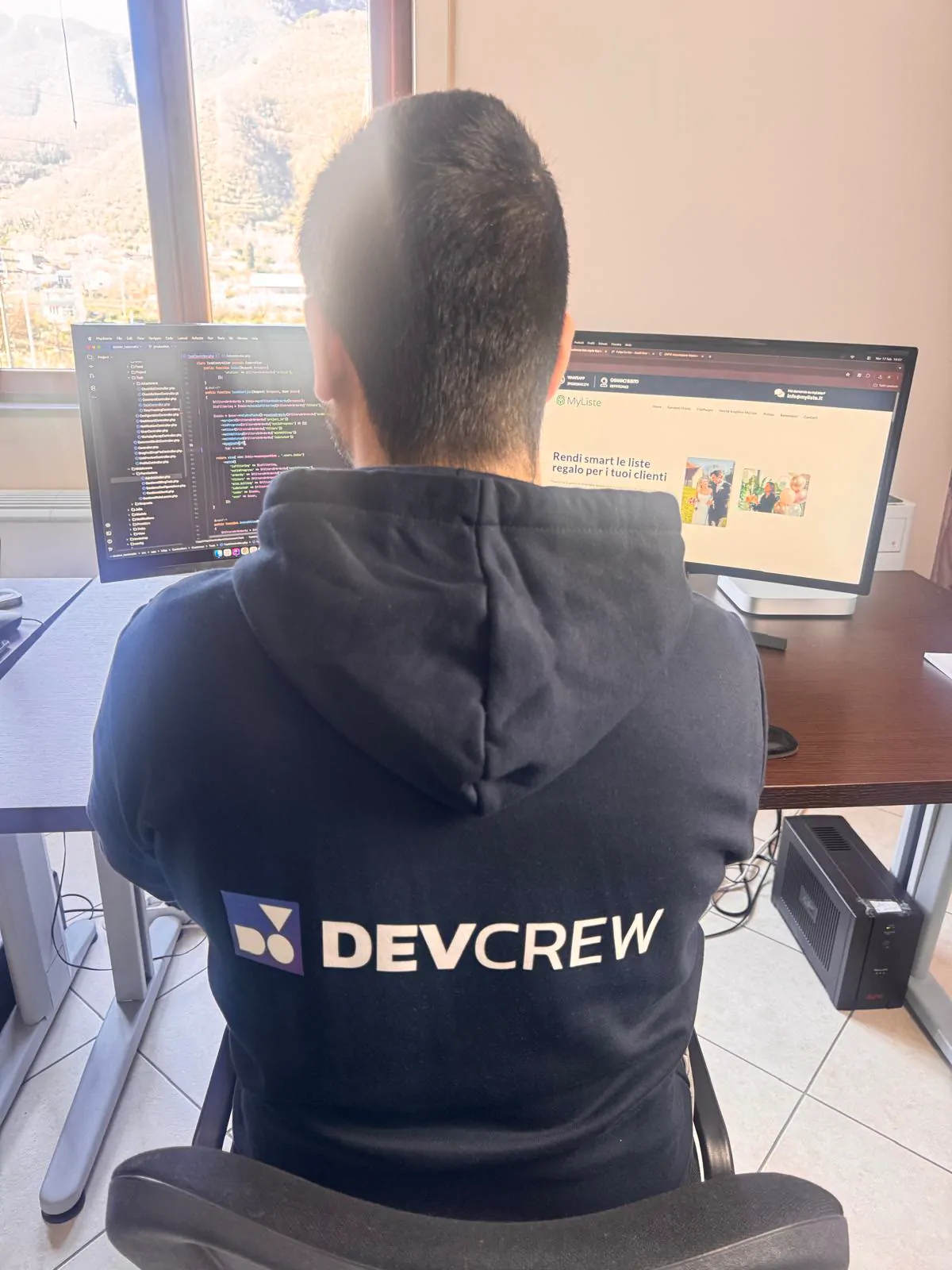 Sviluppatore DevCrew al lavoro su codice e sito MyListe, felpa con logo DevCrew